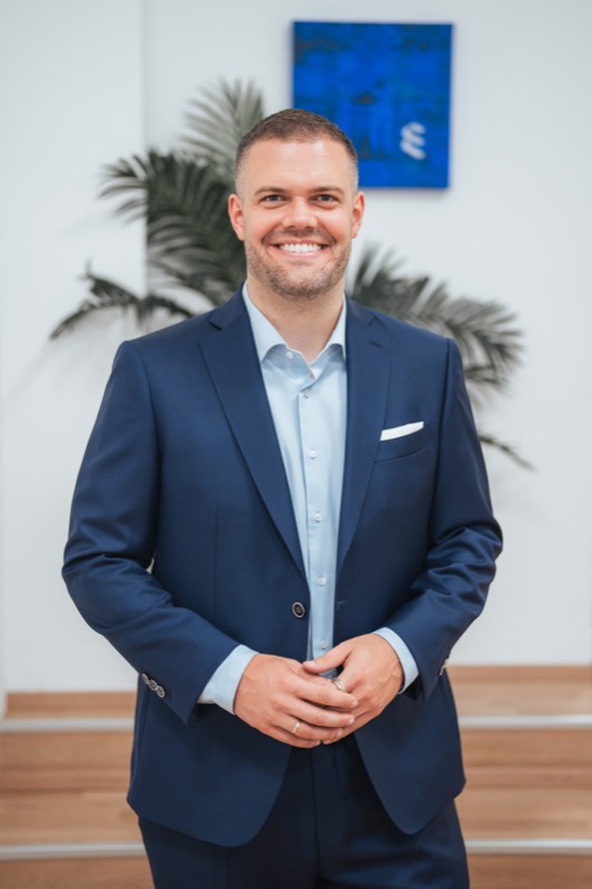 Business-Portrait eines lächelnden Geschäftsführers im dunkelblauen Anzug in einem hellen Büro