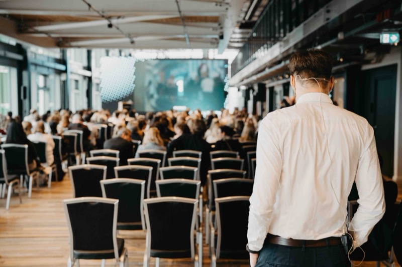 Voll besetzter Konferenzsaal mit Bühne und Leinwand