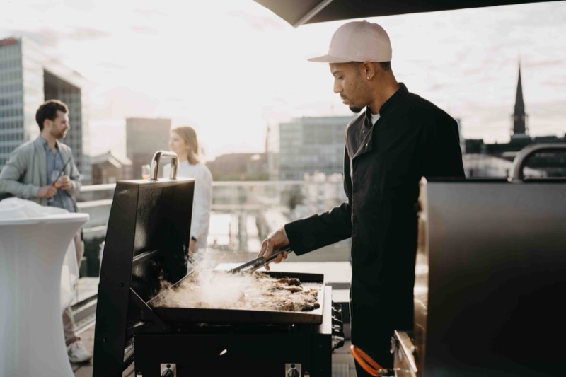 Koch am Grill auf einer Dachterrasse mit Blick über die Stadt